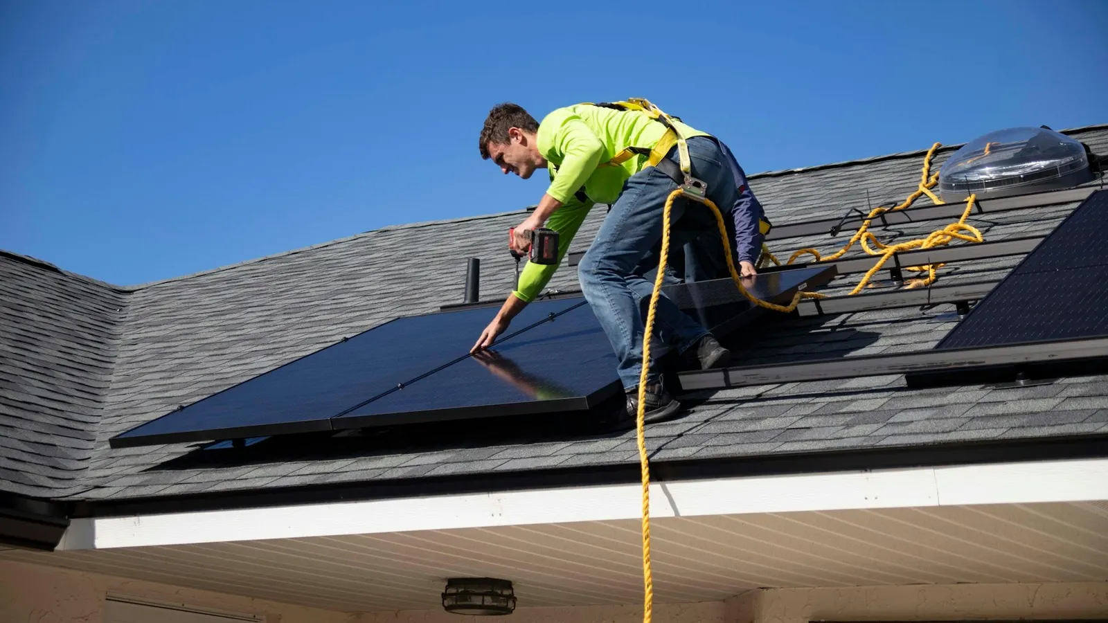 Trabajador con arnés instala paneles solares sobre el techo de una vivienda, con cielo despejado