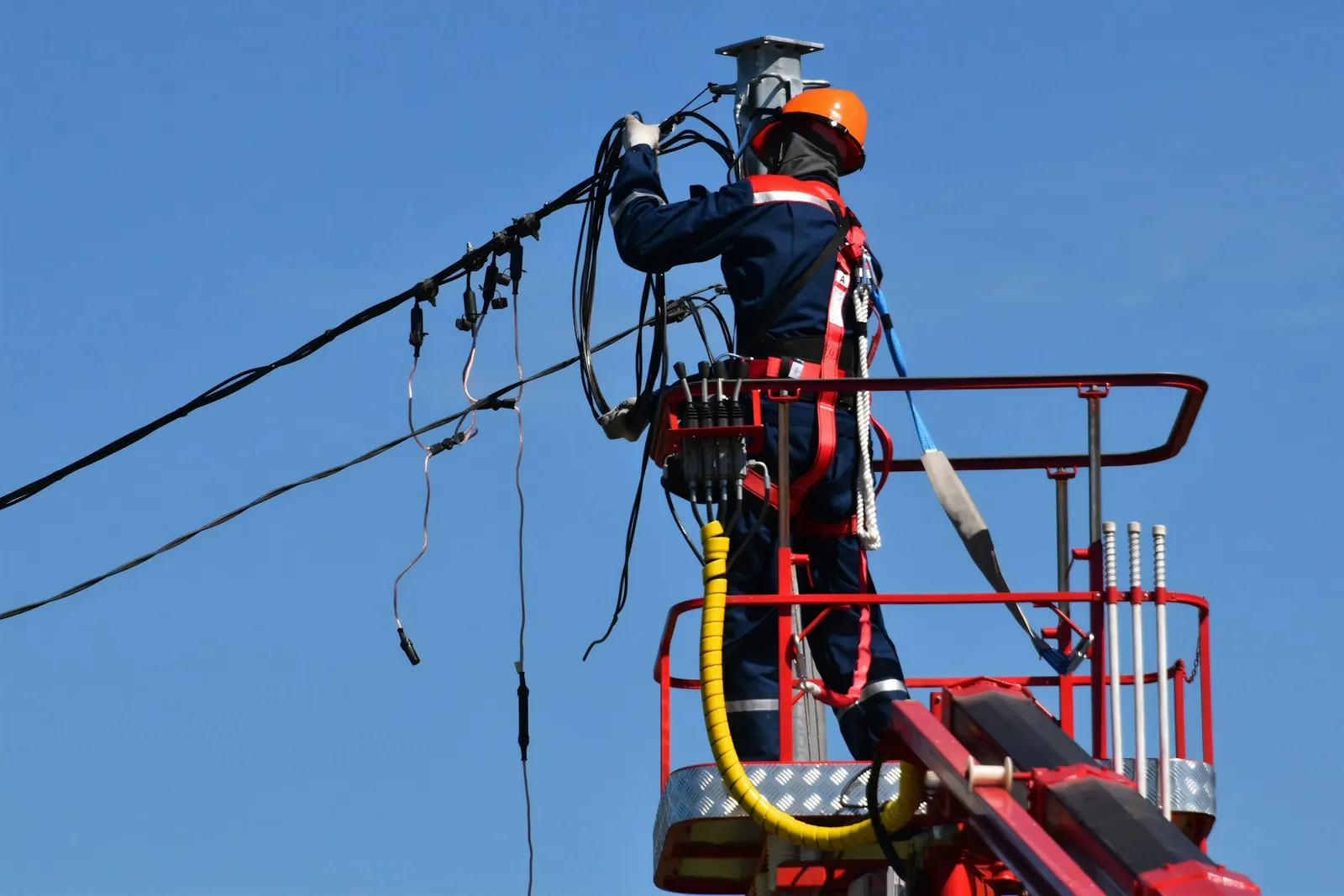 Técnico en un elevador repara cables en lo alto de un poste eléctrico contra el cielo despejado